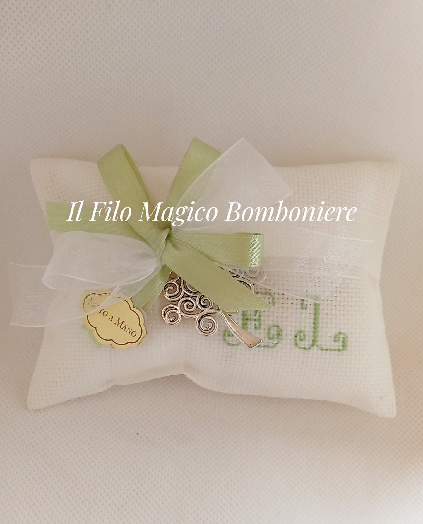 Confezione elegante avvolta in tessuto bianco, decorata con un nastro verde e un piccolo ornamento metallico dai dettagli sinuosi.