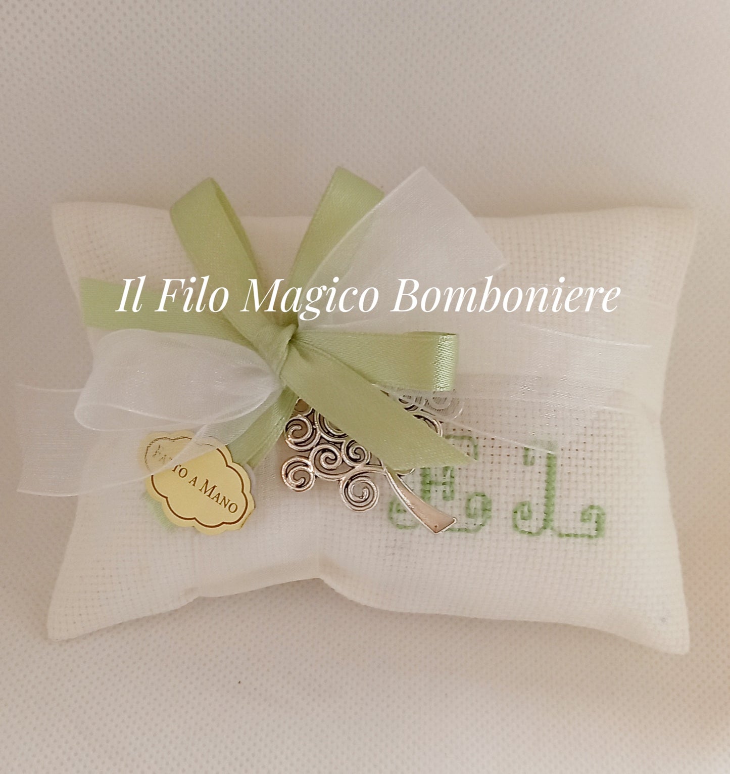 Bomboniera artigianale con un fiocco verde di raso e bianco trasparente, un'etichetta dorata "Fatto a Mano" e un albero argentato simbolico come dettaglio centrale.