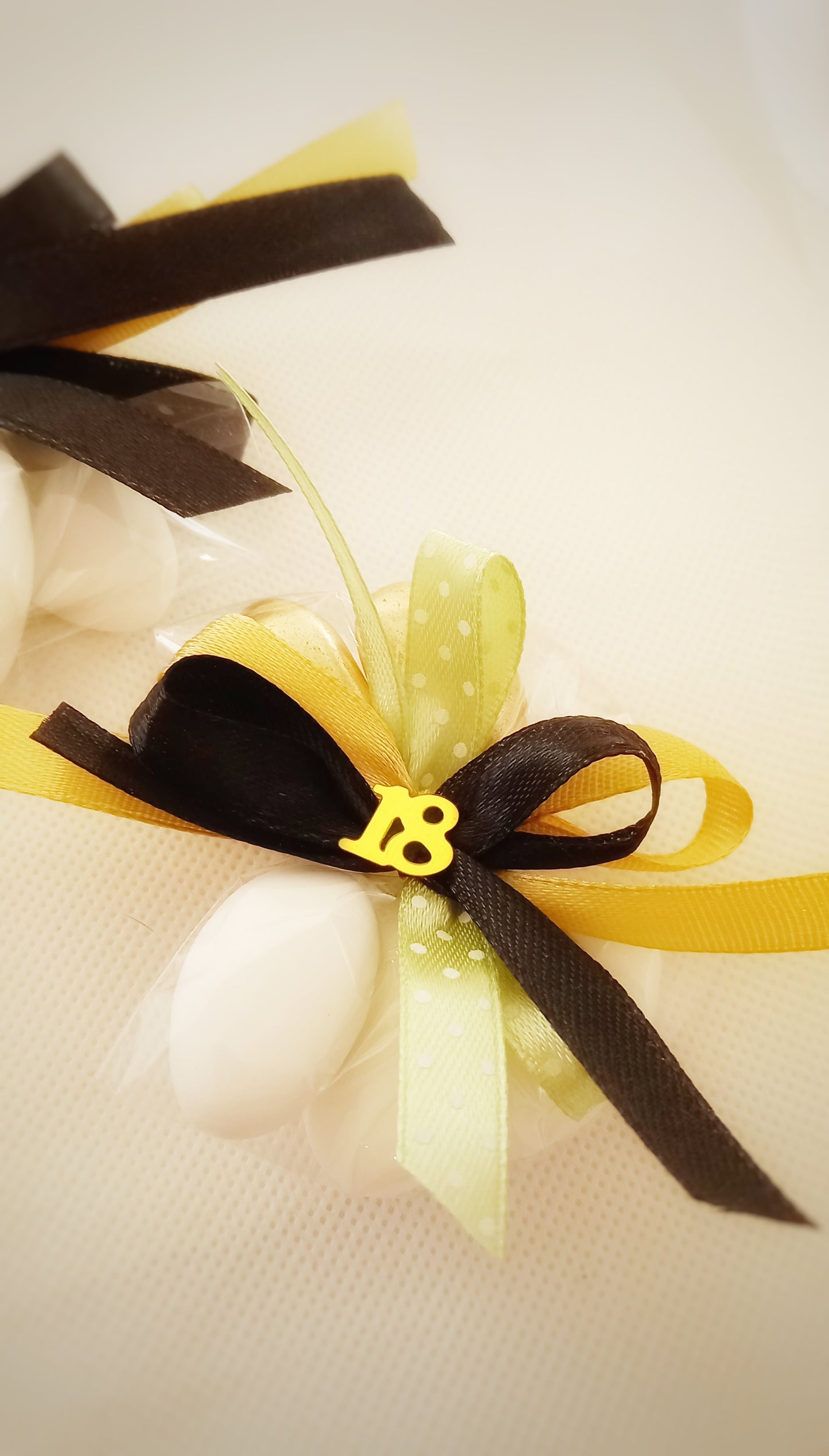 Confezione bomboniera per il 18° compleanno: 5 confetti al cioccolato, 3 bianchi e 2 dorati, chiusi con nastri in vari colori. Decorata con il numero '18' dorato