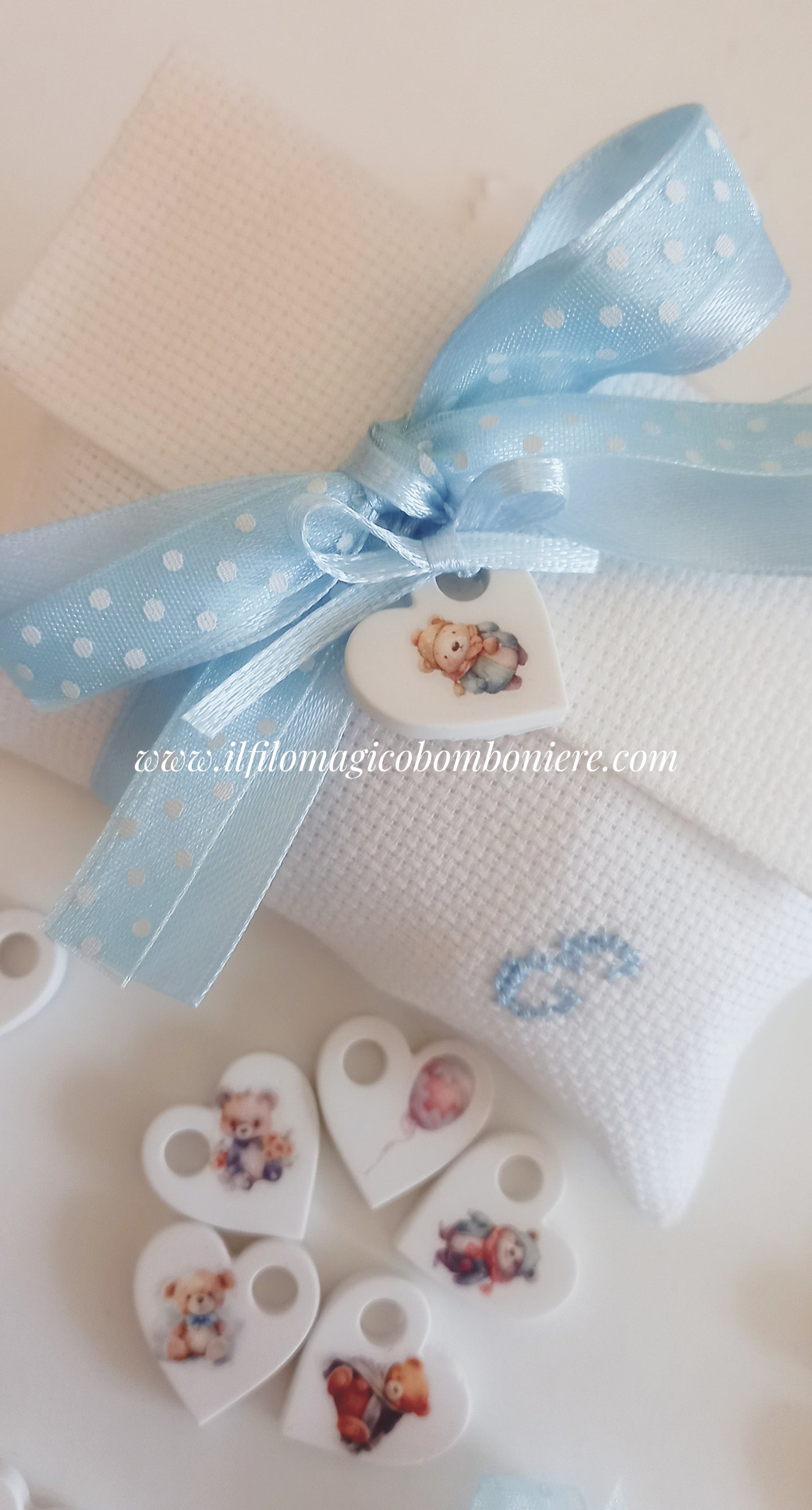 Bomboniera battesimo bimbo: busta bianca con iniziale ricamata e cuoricino in ceramica.