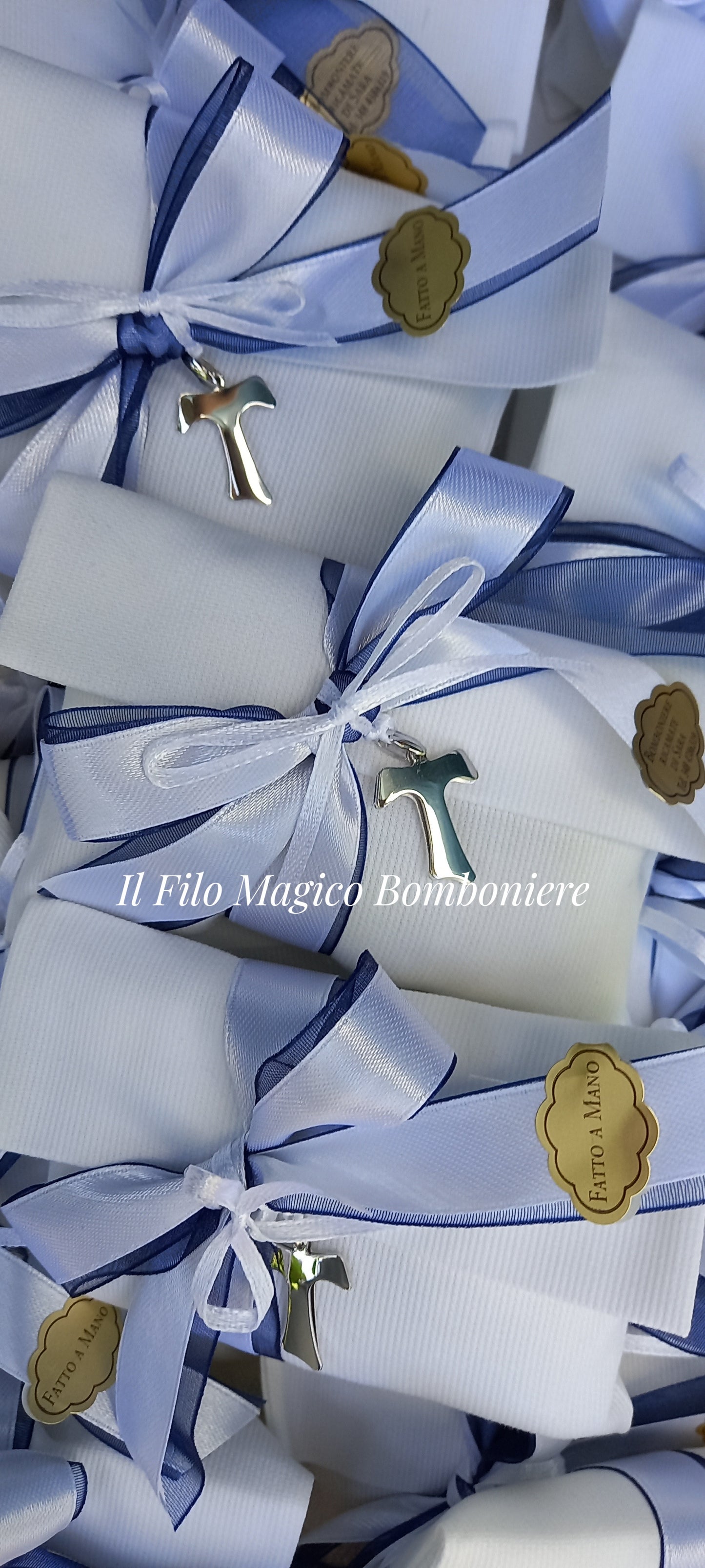 Bomboniera artigianale con croce Tau in argento 925, simbolo di fede e protezione. Rifinita con nastro doppio raso bianco e blu.