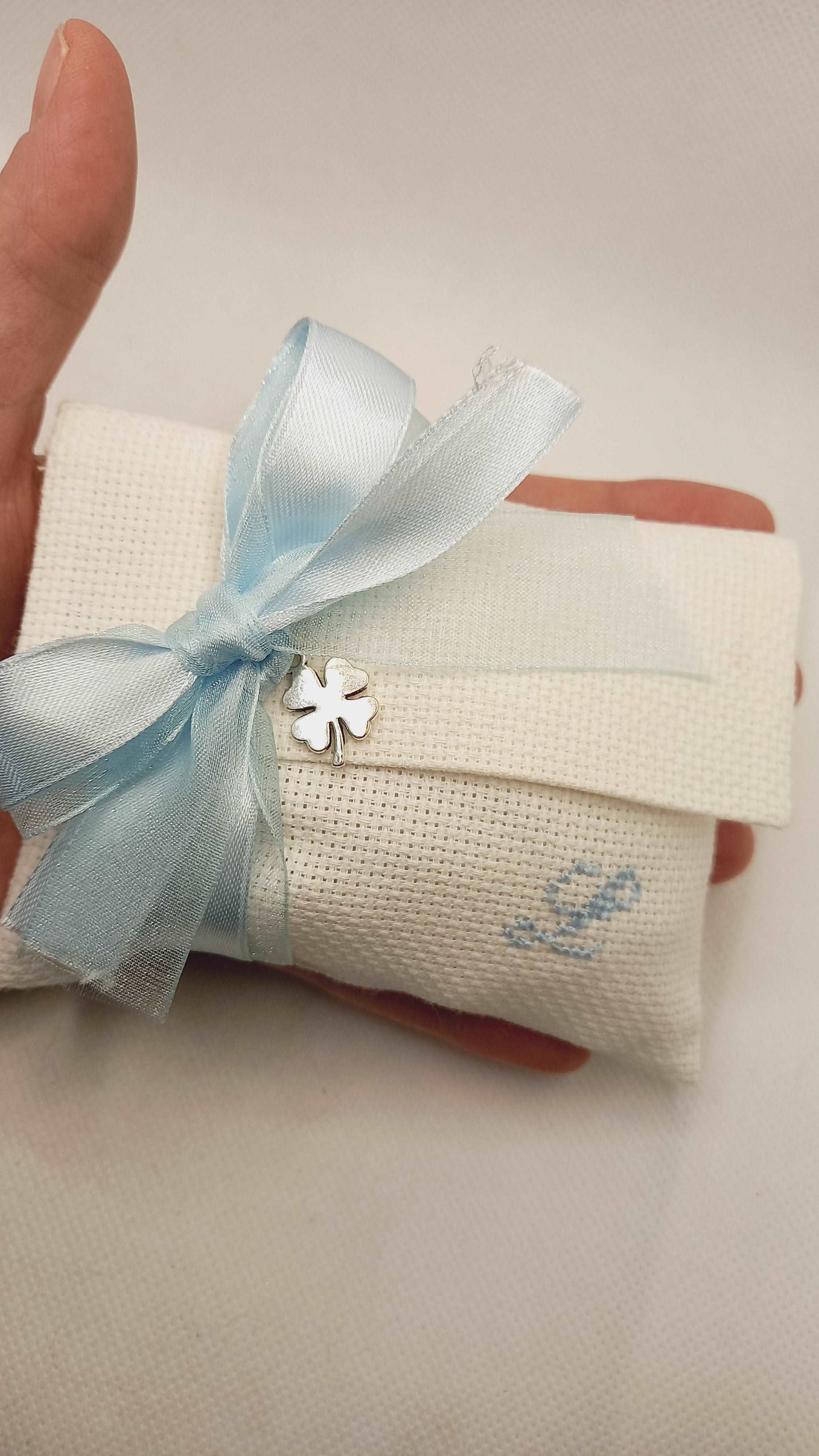 bomboniera battesimo bimbo con busta porta confetti con iniziale del nome ricamata a mano e in abbinamento ciondolo quadrifoglio argentato