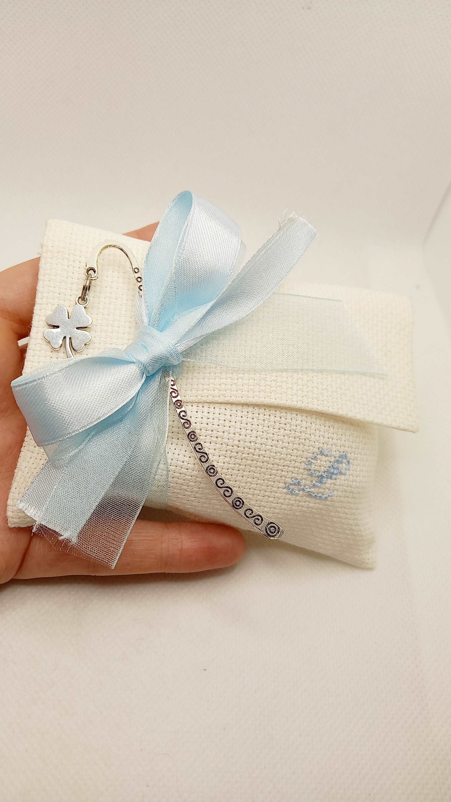 bomboniera battesimo bimbo busta bianca con iniziale del nome ricamata a mano in azzurro nastri raso e organza azzurra segnalibro quadrifoglio