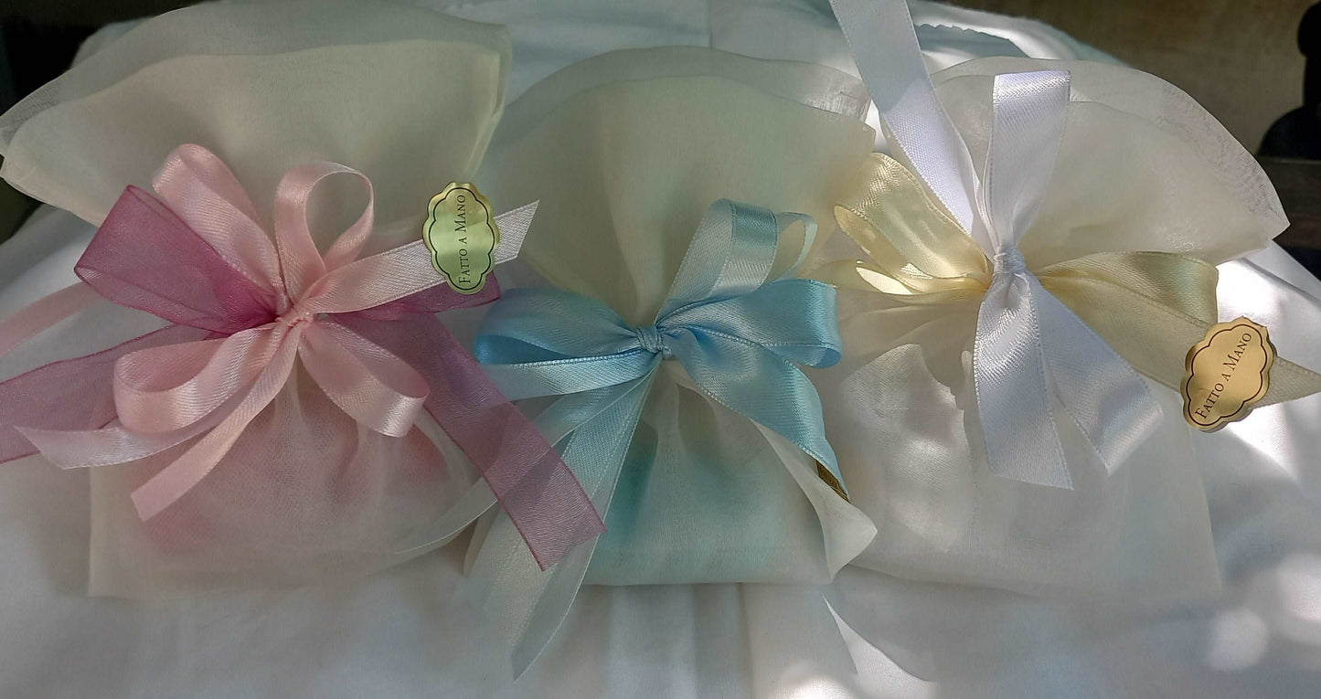 Tre sacchettini porta confetti in organza avorio, ciascuno chiuso con fiocchi colorati( rosa, azzurro e bianco) con etichetta " Fatto a mano "