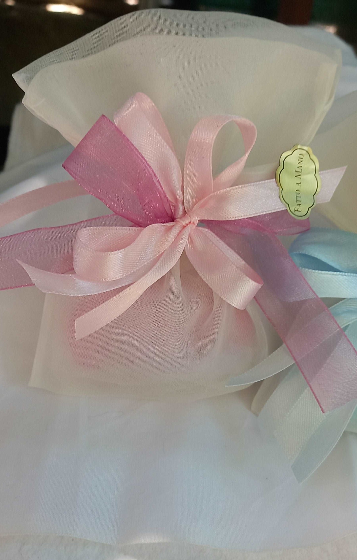 Sacchettino porta confetti in organza avorio chiuso con fiocco rosa e fucsia, etichetta "Fatto a mano " visibile sul lato.