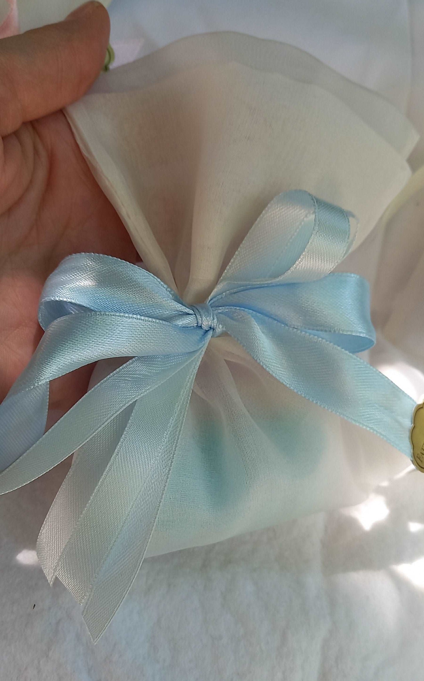 Sacchettino porta confetti in organza avorio chiuso con fiocco azzurro, etichetta "Fatto a mano " visibile sul lato.