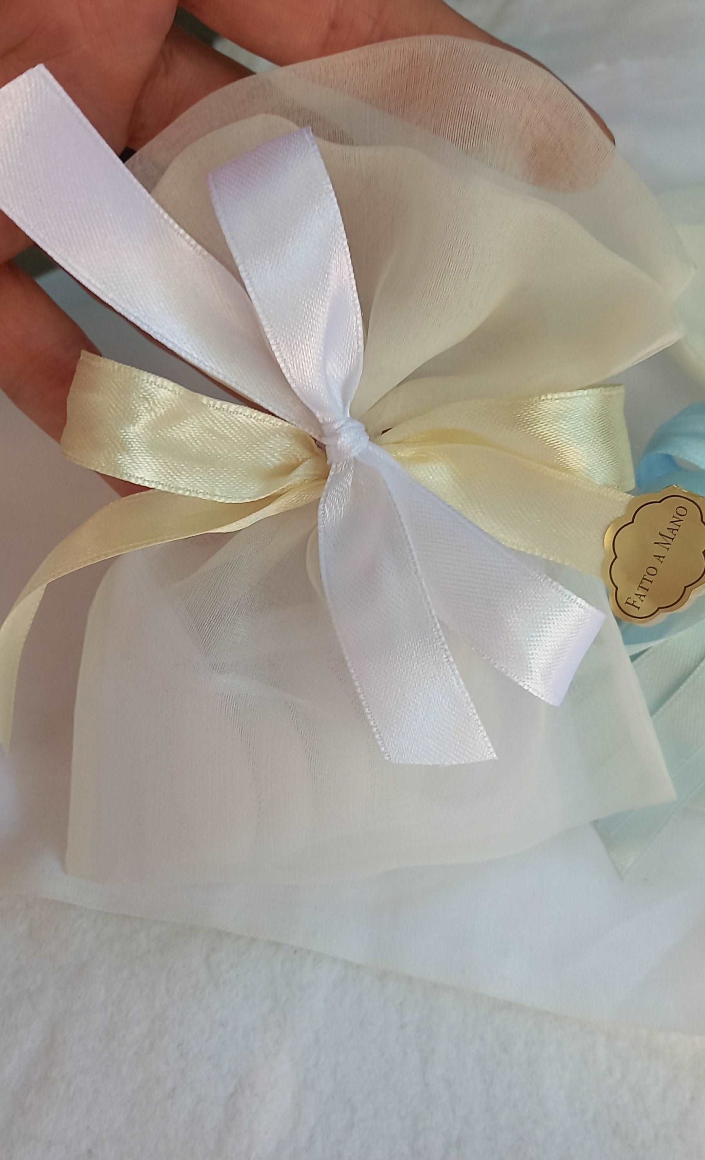 Sacchettino porta confetti in organza avorio chiuso con fiocco bianco ed ecru, etichetta "Fatto a mano " visibile sul lato.