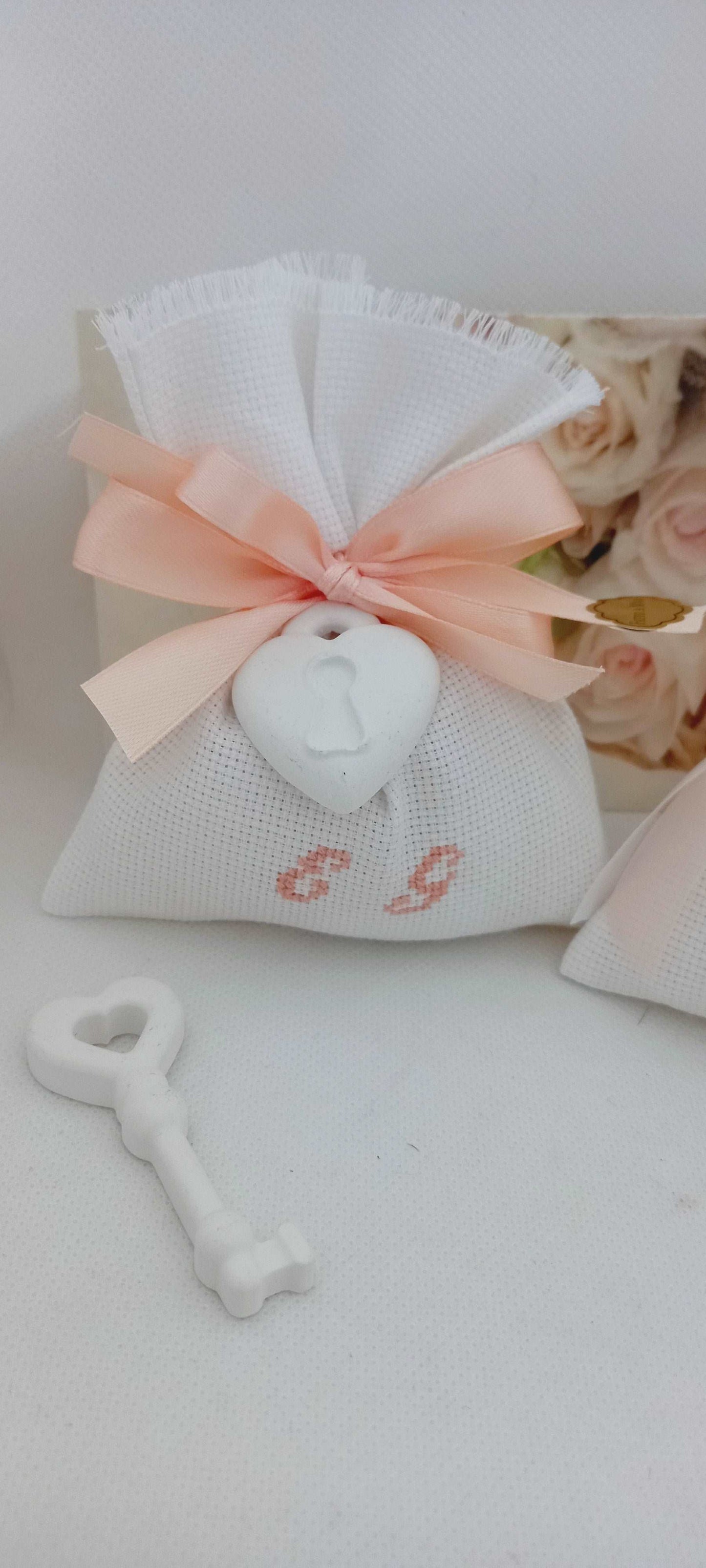 bomboniera matrimonio composta da sacchettino bianco con iniziali ricamate in rosa pesca chiuso con nastri rosa pesca di raso e gessetto cuore lucchetto