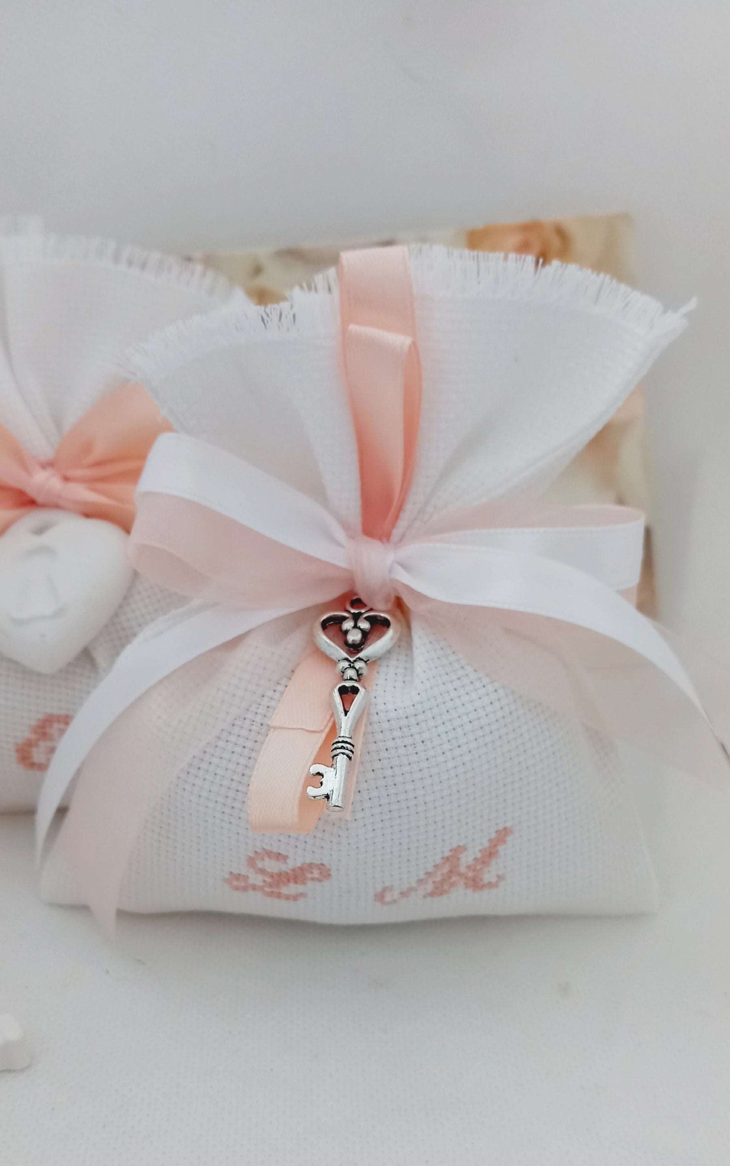 sacchettino per matrimonio bianco con iniziali color rosa salmone chiuso con nastri bianco e rosa salmone e ciondolo chiave argentato
