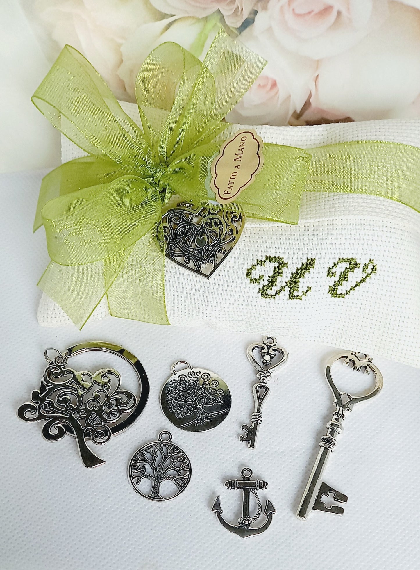 bomboniera nozze busta avorio con iniziali e nastro organza verdi con ciondolo cuore argentato portachiavi albero della vita e ciondoli di varie forme ancora, chiavi e albero della vita.