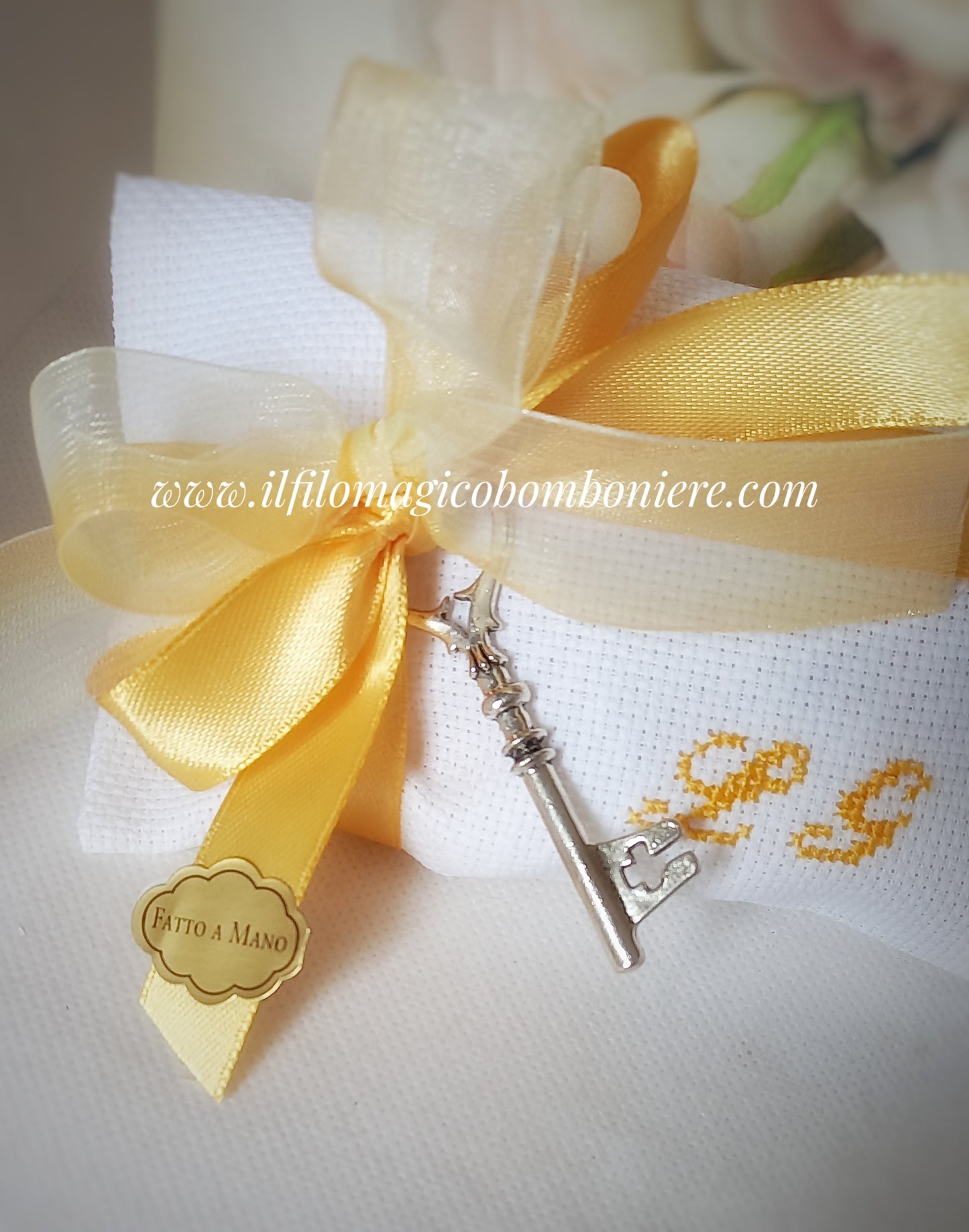 bomboniera nozze oro composta da busta bianca con iniziali dei nomi degli sposi ricamate a mano i giallo oro , chiusa con nastri raso e organza in tinta con il ricamo e ciondolo a forma di chiave