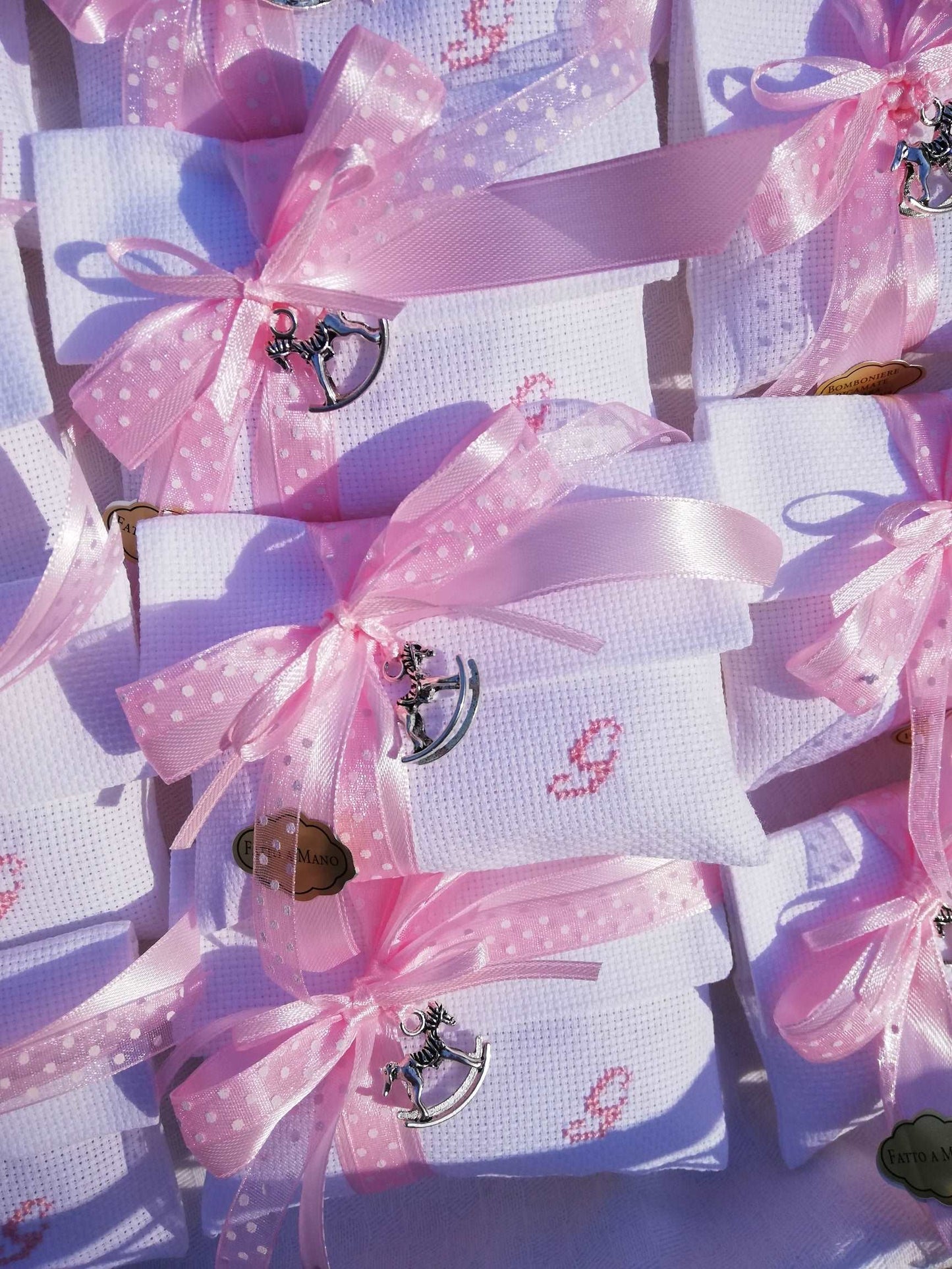 bomboniere battesimo composte da busta bianca con iniziale del nome ricamata in rosa nastri raso e organza pois rosa e ciondolo cavallo a dondolo