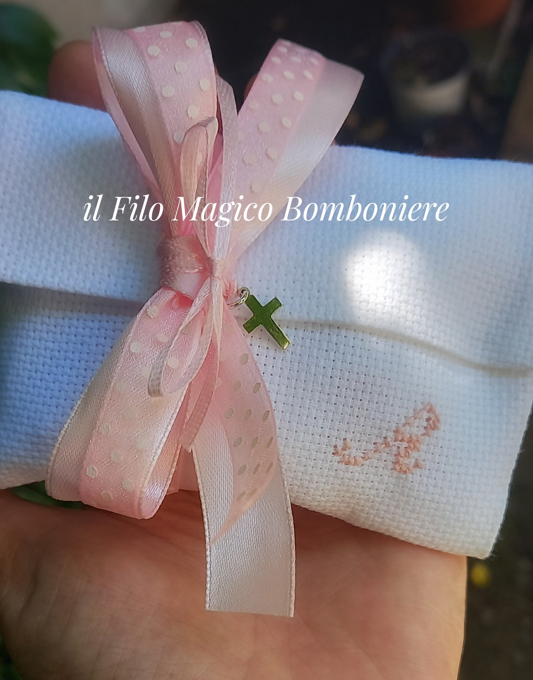 Dettaglio del ricamo rosa e fiocco in organza con croce su bomboniera fatta a mano.