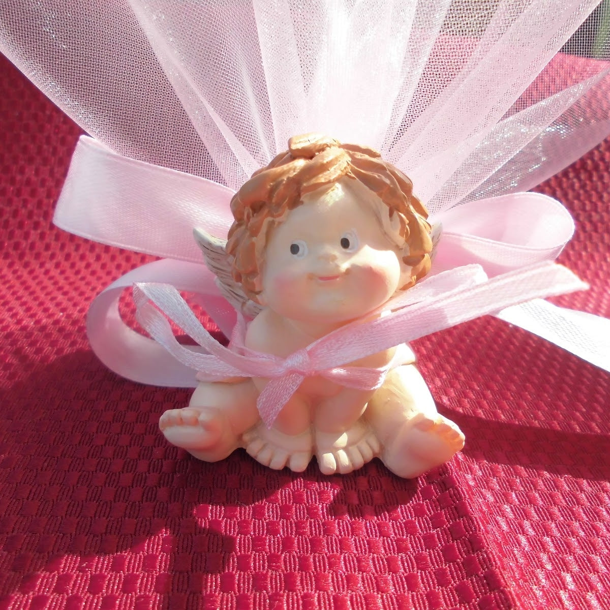 Angioletto in resina dipinta a mano, alto circa 5 cm, di colore rosa, con tulle rosa intorno e cinque confetti al cioccolato Crispo
